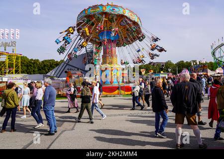 Persone che si divertono all'Oktoberfest e che si divertono sulla giostra della catena. Altri si passeggiare per le strade della zona del festival. Foto Stock