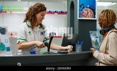 Farmacista femminile aiutare i clienti ad acquistare prodotti medici, vitamine di scansione, integratori e pillole scatole in farmacia. Dipendente medico che lavora presso un negozio di farmaci con farmaci. Foto Stock