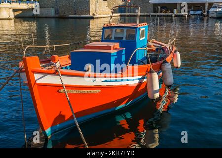 Piccola barca da pesca greca tradizionale arancione, bianca e blu con parabordi ancorata nel nuovo porto di Mykonos all'alba, isola di Mykonos, Grecia. Foto Stock