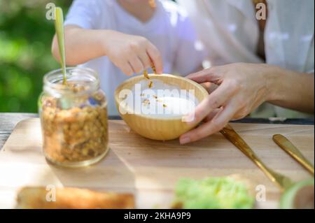 Capretto irriconoscibile che prepara yogurt con granola Foto Stock