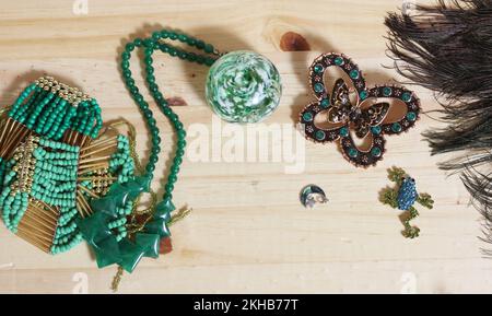 Piume di pavone con perline verdi e broccia di farfalle verde e di rame su tavola di legno Foto Stock