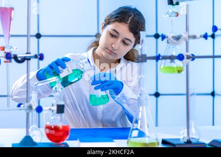 giovane scienziata femminile adulta conduce un esperimento chimico in un laboratorio di sintesi di idrocarburi Foto Stock