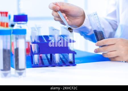 giovane donna adulta in un laboratorio chimico conduce un'analisi chimica di campioni di terreno di un campo agricolo Foto Stock