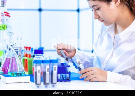 giovane donna adulta in un laboratorio chimico conduce un'analisi chimica di campioni di terreno di un campo agricolo Foto Stock