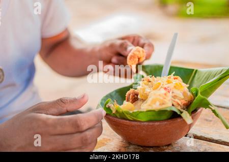 Primo piano della persona che mangia tonificante sul tavolo. Persona locale che mangia una vigorón tradizionale. Il rinvigorente cibo tipico di Granada, concetto di cibo tipico di Foto Stock