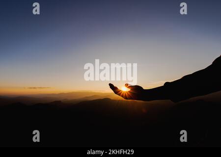 silhouette di uomo alzarsi mano in preghiera in cima alla montagna e tramonto cielo sfondo astratto. Concetto di libertà e avventura di viaggio. Foto Stock