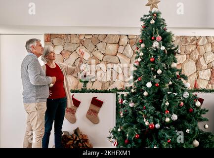 Donna anziana e uomo, albero di natale decorazione con pianificazione, parlare o discussione in casa. Coppia anziana, decorazione interna e vacanza Foto Stock