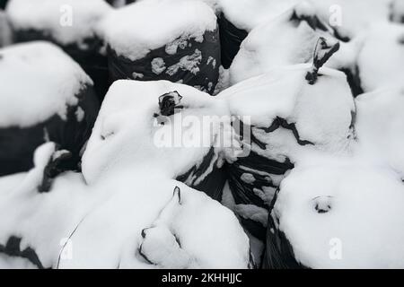 Mucchio di sacchi di spazzatura neri all'aperto sotto la neve. Sacchetti per rifiuti neri grandi e densi con immondizia raccolta. Pulizia del territorio e dell'ambiente da Foto Stock