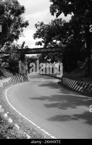 Foto in bianco e nero, foto monocromatica di una strada tortuosa abbandonata che viene raramente passata dai veicoli a Pangandaran - Indonesia Foto Stock