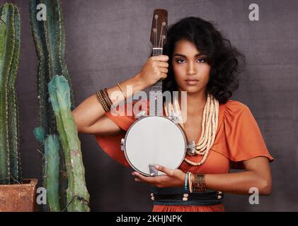 Lascia che ti riproduci una canzone. Studio ritratto di una bella giovane donna etnica in possesso di un banjo mentre in piedi accanto a cactus. Foto Stock