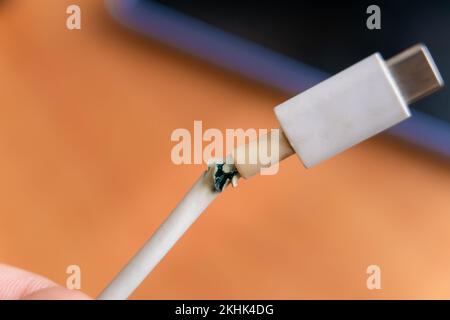 Primo piano tra il cavo del caricabatteria di tipo C bianco rotto e il telefono. Il cavo USB è danneggiato. Foto Stock
