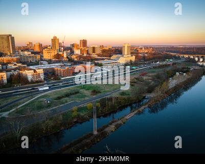 Una vista drone di uno skyline della citta' con un fiume circondato da edifici e natura all'alba a New Brunswick, Rutgers, Hub City, USA Foto Stock