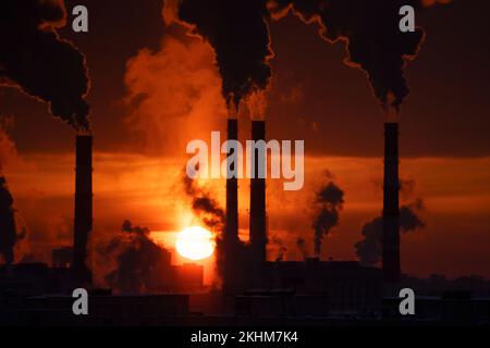 Centrale elettrica a carbone con camini fumanti contro il cielo rosso del tramonto. Inquinamento atmosferico nella città invernale Foto Stock