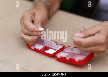 Le mani di donna anziana prendono le pillole dalla scatola. Assistenza sanitaria e concetto di vecchiaia con farmaci. Medicamenti a tavola Foto Stock