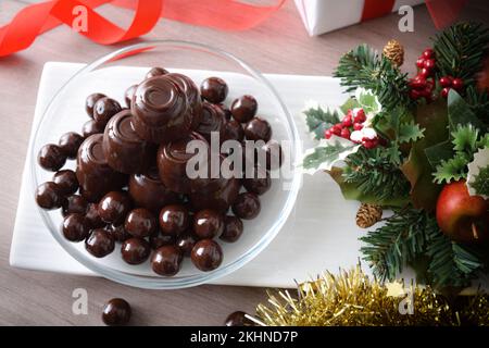 Piatto con pila di cioccolatini e palline di cioccolato fondente su tavolo di legno e decorazione natalizia. Vista dall'alto. Foto Stock