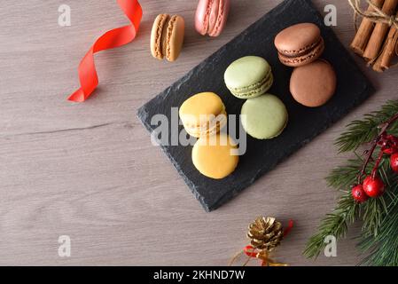 Macaroni francesi di vari sapori su un piatto di ardesia su tavola di legno con decorazioni natalizie. Vista dall'alto. Foto Stock