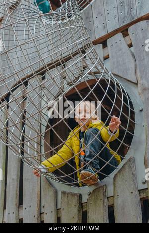 Un bambino sale su una griglia alpina in un parco giochi in una calda giornata estiva. parco giochi per bambini in un parco pubblico, intrattenimento e svago Foto Stock