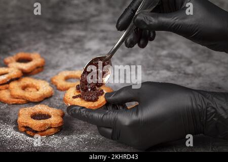 Biscotti natalizi Linzer. Il confetter con guanti riempie i biscotti con marmellata di prugne. Dolci fatti in casa Foto Stock