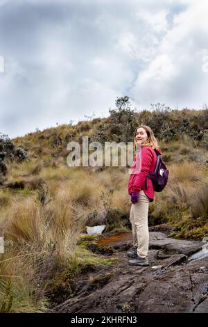 Foto integrale verticale di una ragazza che guarda tranquillamente la macchina fotografica nel Parco Nazionale di Cajas negli altopiani dell'Ecuador, Cuenca, Ande tropicali. Foto Stock