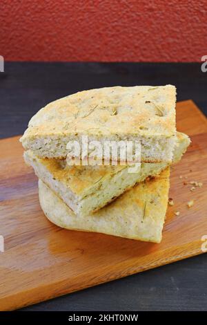 Pila di fette di focaccia italiana alle erbe appena sfornate su un panetto di legno Foto Stock