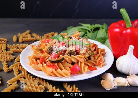 Fusilli crudi appena cotti in salsa di pomodoro sul tavolo da cucina con i suoi ingredienti Foto Stock