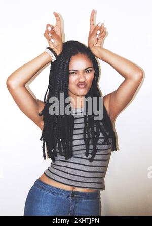 Ritratto, gesto della mano e corna con una donna nera in posa in studio su uno sfondo grigio per un divertimento stravagante. Viso, moda e bellezza con un attraente Foto Stock