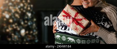 donna che dà un abbraccio di ringraziamento a suo marito dopo aver ricevuto una scatola regalo. coppia romantica che festeggia la vigilia di natale a casa. banner con spazio di copia Foto Stock