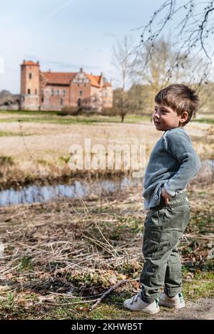 Il bambino pensivo prende una pausa ammirando un prato stupefacente vicino ad un castello. Contemplativo, bambino in piedi che riposa nella natura trasmette il concetto di contemplazione Foto Stock