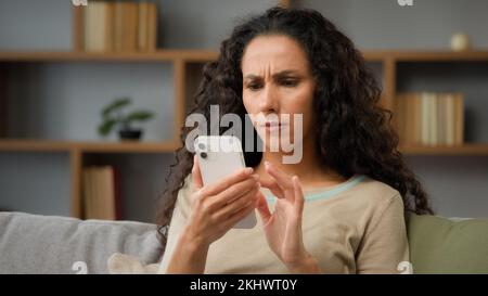 Closeup arrabbiato confuso sconcertato stressato nervoso donna adulta guardando lo schermo del cellulare a casa ha problemi con la connessione wi-fi sensazione frustrato di Foto Stock