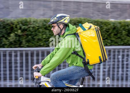 Consegna rapida uomo in città, giovane corriere vestito con abbigliamento tecnico e sportivo, con casco e zaino per cibo, effetto panning, veloce Foto Stock