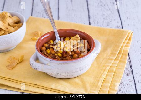 Una zuppa di coccio ripiena di peperoncino con carne e sormontata con patatine di mais. Foto Stock