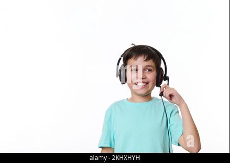 Bambino adolescente ispanico intelligente, scolaro che indossa cuffie audio, sorride un sorriso allegro e toothy, isolato su bianco Foto Stock