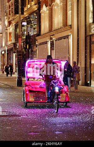 Pedicab aka Rickshaw con luci al neon in una notte d'inverno a New Bond Street, quando la neve finta cade intorno. Londra Foto Stock