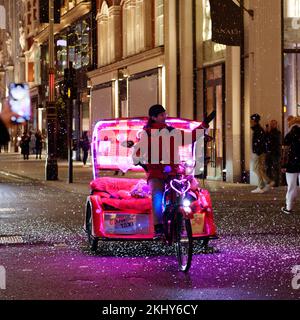 Pedicab aka Rickshaw con luci al neon in una notte d'inverno a New Bond Street, quando la neve finta cade intorno. Londra Foto Stock