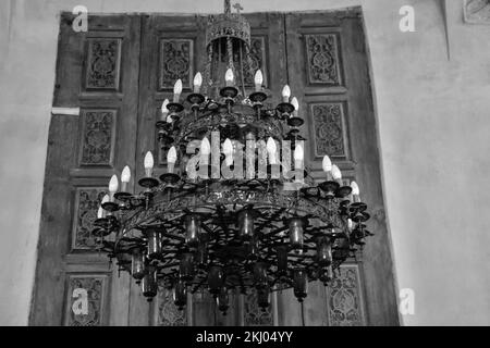 Un'immagine in scala di grigi di un antico lampadario di un antico Monastero Egiziano contro una porta d'epoca Foto Stock