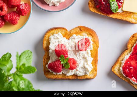 Panino aperto con fette di pane Brioche, ricotta, lamponi freschi e menta Foto Stock