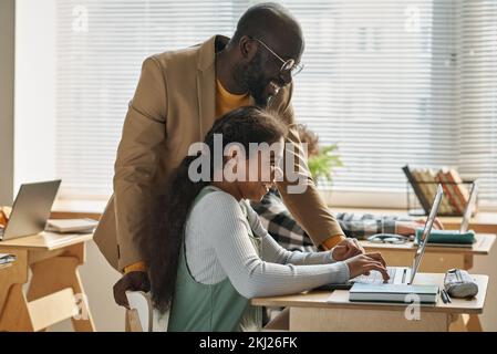 Insegnante afroamericana che parla con uno studente e le mostra come lavorare al computer durante una lezione in classe Foto Stock