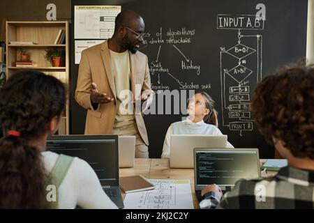 Uomo afroamericano che insegna ai giovani sviluppatori di usare un programma informatico a lezione Foto Stock