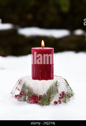 Portacandele natalizio fatto a mano a forma di torta di ghiaccio, bacche di rosa rossa, rami di bacche agrifoglio e rametti di thuja con candele brucianti Foto Stock