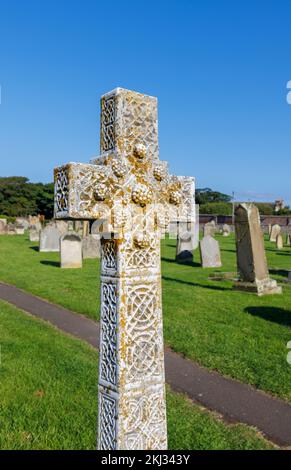 Croce commemorativa in pietra arrugginita di lichen nella chiesa di St Aidan a Bambburgh, un villaggio nel Northumberland sulla costa nord-orientale dell'Inghilterra Foto Stock