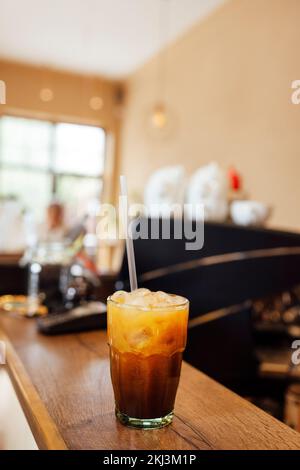 Caffè ghiacciato con arancia. Bicchiere di americano mescolato con soda artigianale e succo d'arancia yuzu su sfondo sfocato, rinfrescante concetto di bevanda estiva. Foto Stock