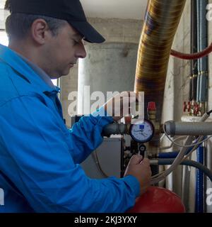 Idraulico in abiti da lavoro riparazione e manutenzione di una caldaia di casa. Accendere la caldaia in previsione dell'inverno Foto Stock