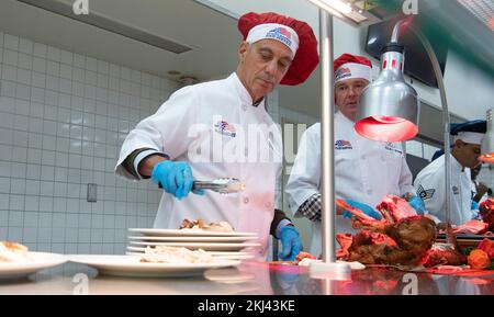 Fussa, Giappone. 24th Nov 2022. STATI UNITI Ambasciatore in Giappone Rahm Emanuel, a sinistra, e negli Stati Uniti Ricky Rupp, a destra, Comandante delle forze Giappone, vestito in uniformi chef, serve prosciutto e turchia per servire i membri durante il giorno del Ringraziamento al Samurai Cafe Dining Facility presso la base aerea di Yokota, il 24 novembre 2022 a Fussa, Giappone. Credito: TSgt. Christopher Hubenthal/US Air Force/Alamy Live News Foto Stock