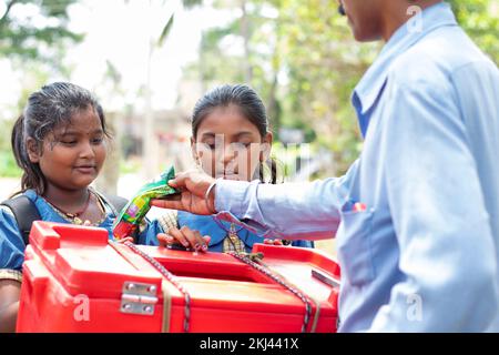 Scuola Bambini acquisto di ghiaccio lolly con gelato venditore in villaggio Foto Stock