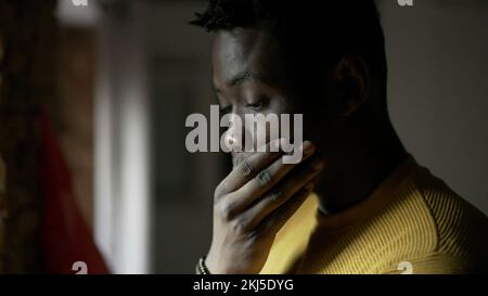 Uomo africano in piedi dalla finestra pensando alla vita. Preoccupata emozione preoccupata Foto Stock