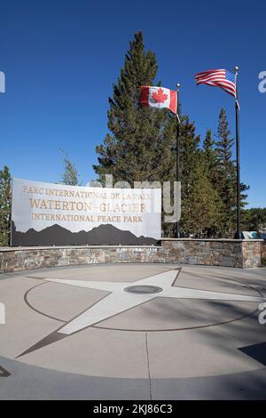 Bandiere canadesi e americane che volano sopra il Waterton-Glacier International Peace Park plaza ad Alberta, Canada. Il primo parco internazionale di pace al mondo Foto Stock