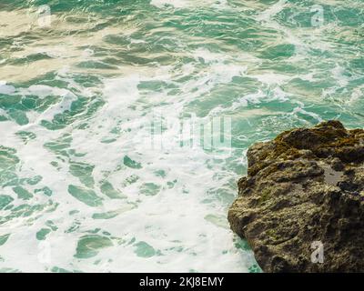 Grande masso nell'oceano. L'acqua turchese con le onde bianche schiumose batte contro una pietra. La bellezza e la maestosità della natura. Deserto, ecologicamente pulito Foto Stock