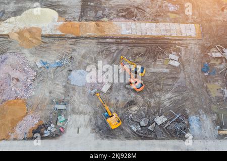 Tre trattori di escavatore su colonne portanti nella fossa della fondazione durante la costruzione della fondazione dell'edificio, scavando. Vista dall'alto dell'antenna Foto Stock