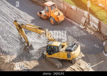 L'escavatore giallo sulle macerie lavora su strade asfaltate, accanto ad esso si trova un impilatore di asfalto Foto Stock