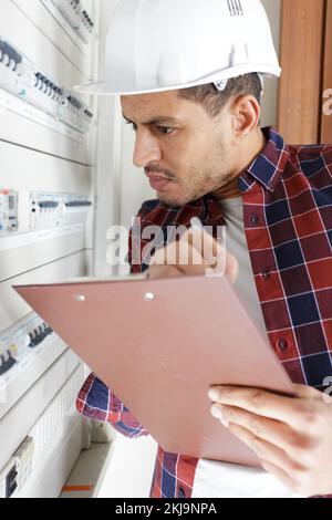 tecnico elettrico che controlla la scatola dei fusibili prendendo appunti Foto Stock